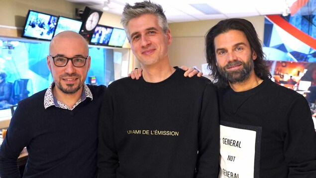 Les trois hommes sont debout, côté à côte.