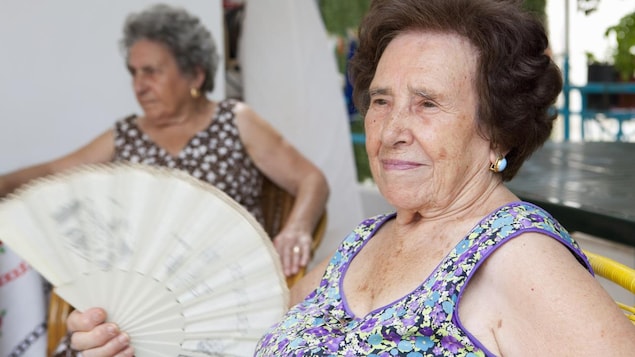 Une femme âgée agite un éventail.