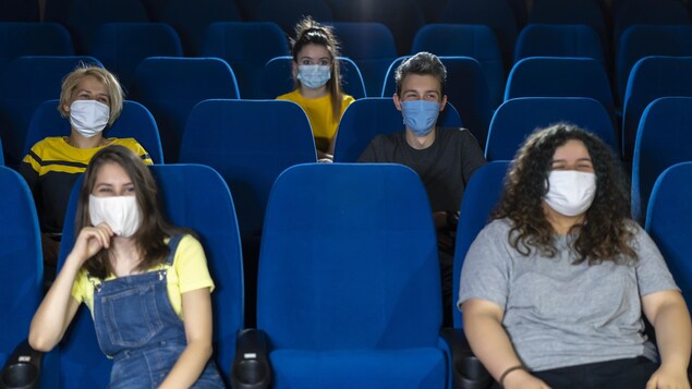 Quelques spectateurs portant des masques assis dans une salle de spectacle pratiquement vide.