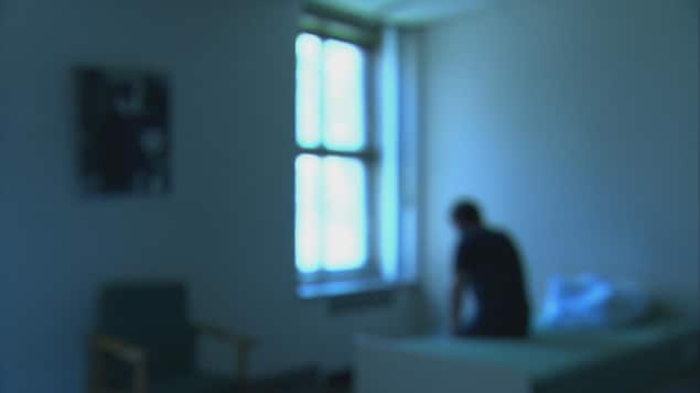 Une image floue d'un homme assis sur un lit dans une petite chambre d'hopital.