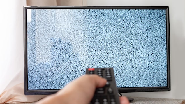 Une main tient une télécommande devant une télé qui n'affiche pas d'image. 