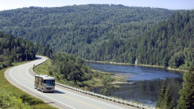 Un véhicule récréatif circule sur une route entourée de montagnes et près d'une rivière.