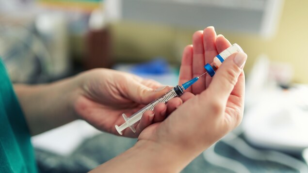 Gros plan sur les mains d'une personne manipulant une seringue et une fiole de vaccin contre la COVID-19. 