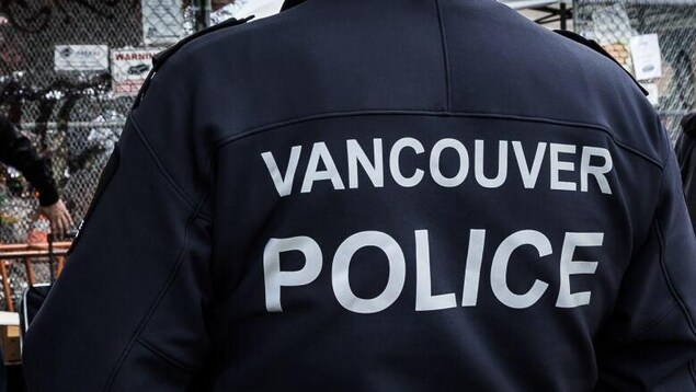 Un homme de dos porte un chandail sur lequel il est écrit Vancouver Police