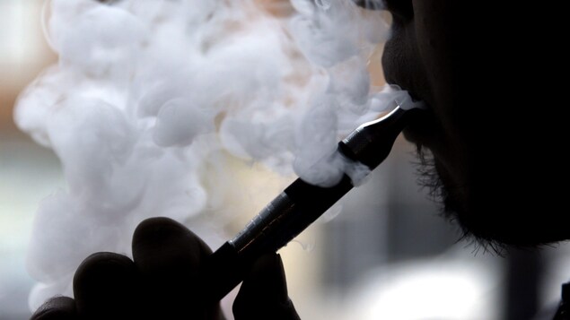 Un jeune homme fume une cigarette électronique.