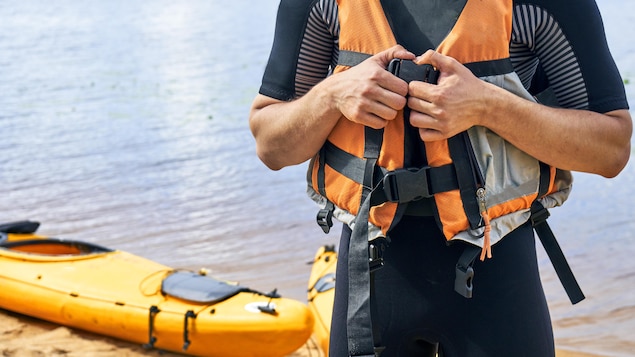 Un kayakiste est en train d'attacher sa veste de flottaison sur le bord d'un lac.