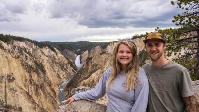 Un couple pause devant un canyon avec une chute au loin.