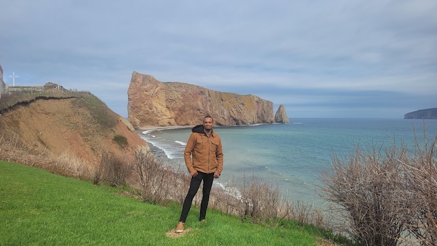 Le jeune homme est photographié devant le rocher Percé, en Gaspésie.