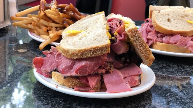Un sandwich au pastrami avec une assiette de frites et un sandwich de boeuf salé en arrière-plan.