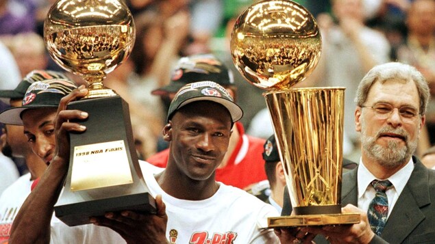 Michael Jordan et l'entraîneur Phil Jackson hissant des trophées après avoir remporté leur sixième championnat en juin 1998.