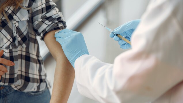 Une personne qui tient un vaccin et qui frotte le bras d'une femme avec une lingette désinfectante.