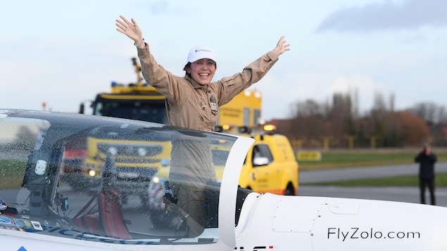 La jeune pilote, debout dans le cockpit de son appareil ultraléger, réagit en levant les bras dans les airs, souriante, après avoir atterri à la fin de son tour du monde en solitaire dans sa ville natale belge de Courtrai, le 20 janvier 2022.