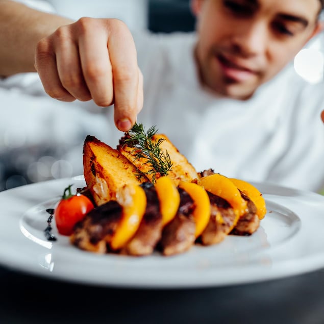 Un chef cuisinier fait le montage d'un plat au premier plan.
