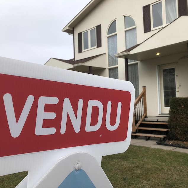 Une pancarte de maison indique «Vendu». À l'arrière-plan se trouve une maison de banlieue.