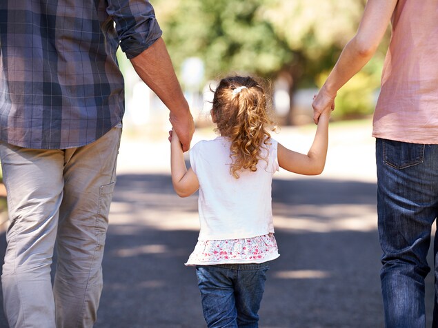 Vue arrière d'une fille qui tient la main de ses parents en marchant dans la rue. Vue arrière d'une fille qui tient la main de ses parents en marchant dans la rue.