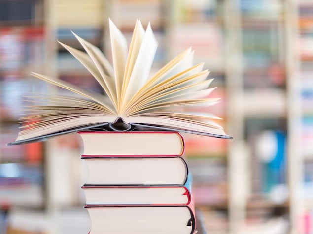 Un livre ouvert sur une pile de livres fermés. 