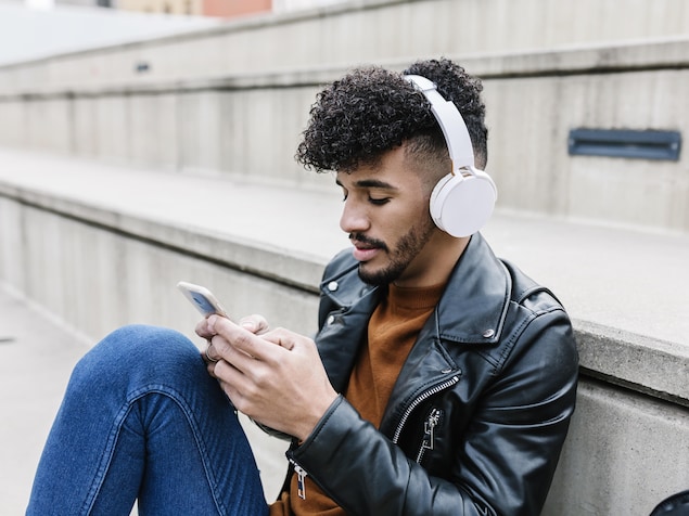 Un homme assis à l'extérieur écoute de la musique avec des écouteurs sur les oreilles. 
