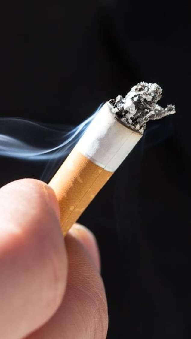 Une main tient un mégot de cigarette allumée.
