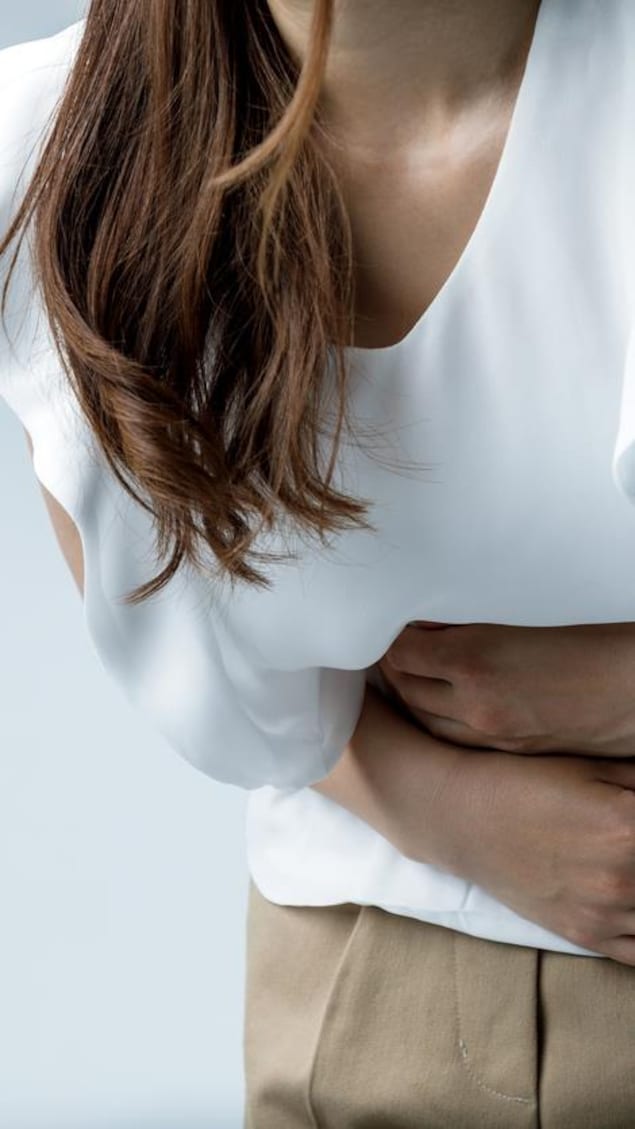 Une femme se tient l'abdomen en raison de douleurs.