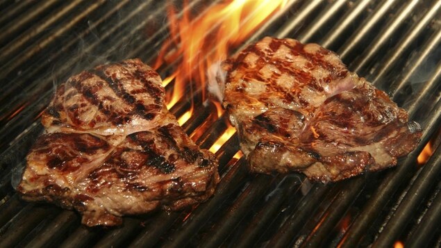Des steaks léchés par les flammes sur la grille d'un barbecue.