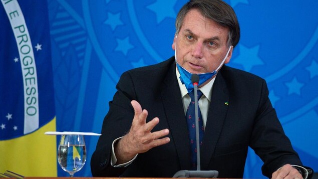 Le président du Brésil est assis. Il porte un masque, mais il l'a baissé pour mieux parler aux journalistes.
