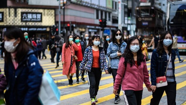 Des piétons portant des masques traversent une rue. 