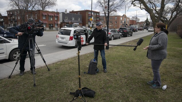 Un journaliste tenant une perche fait une entrevue avec une femme alors que le caméraman se tient à bonne distnce en retrait.