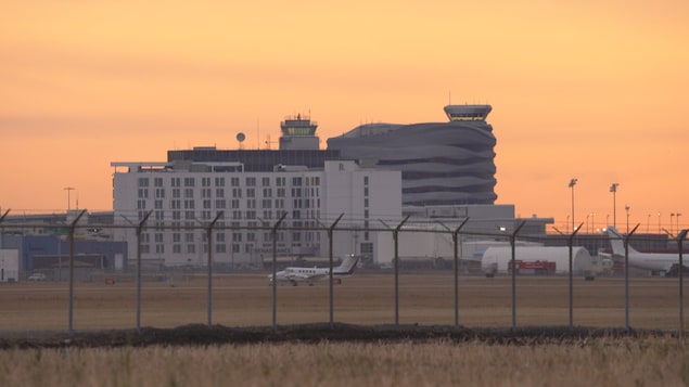 Petit avion blanc en avant plan. En arrière plan des bâtiments de l'aéroport sous fond de ciel orangé. Novembre 2024.