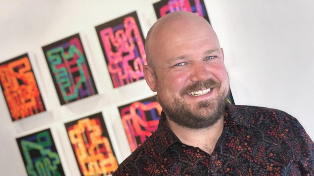 Benjamin Rodger, souriant, devant des toiles sur un mur de galerie.
