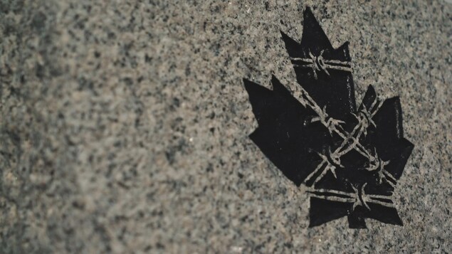 Feuille d'érable noire entourée de barbelés peinte sur une plaque de granite.