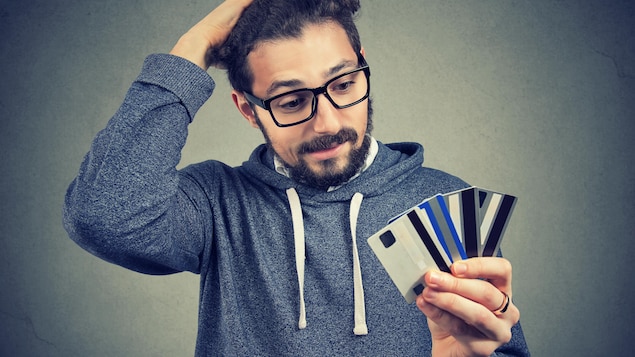 A man who looks desperate holds several credit cards in his hand.