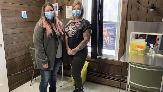 Amélie Roy-Ayotte et Amélie Lechasseur se tiennent devant des tables. Sur ces tables se trouvent des bacs de récupération des seringues souillées.