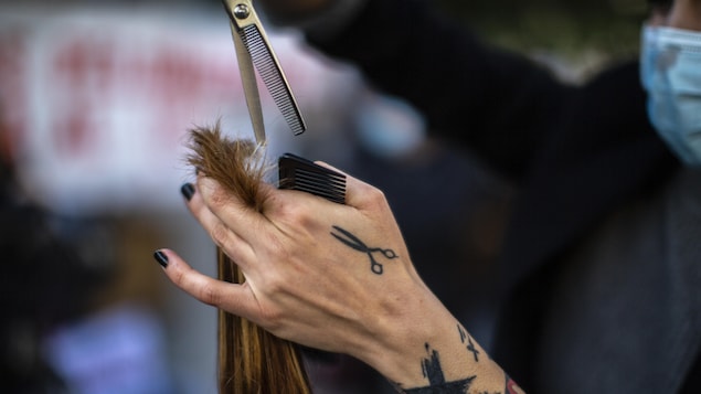 Une coiffeuse coupe les cheveux d'une femme.