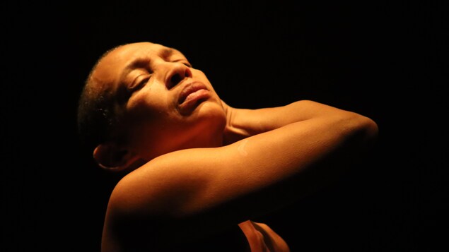 Une femme qui pointe son visage vers le haut en tenant son cou avec son bras.