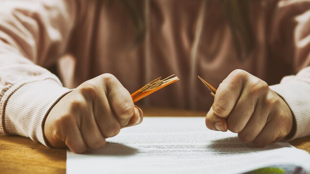 Une personne tient deux bouts de crayon brisé les poingts fermés devant une feuille de papier.