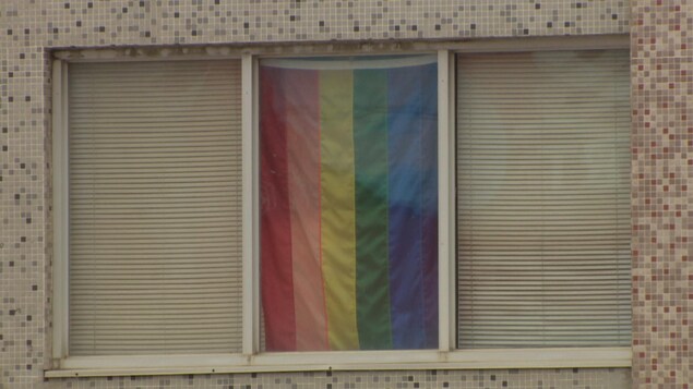 Un drapeau aux couleurs de la communauté LGBTQ est affiché dans une fenêtre.