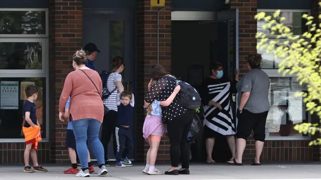 Des parents embrassent leurs enfants à l'extérieur de l'école.