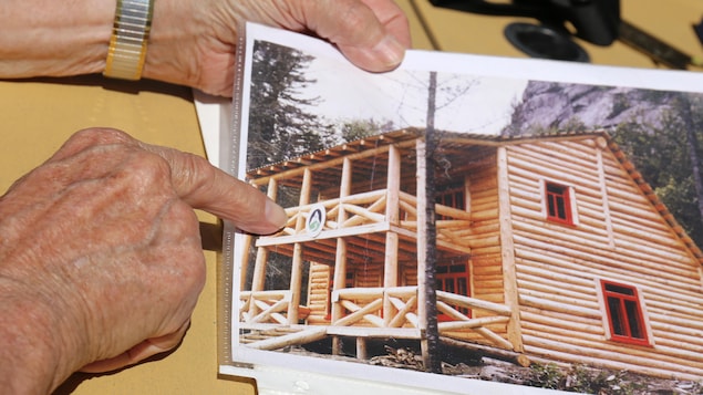 Des mains pointe une photo d'archives sur laquelle on voit un chalet en bois rond.