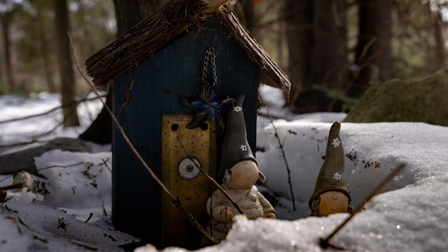 Des petits lutins devant une petite cabane bleue installée dans la neige dans la forêt.
