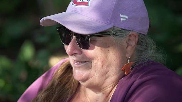 Gros plan d'une femme souriante avec des lunettes fumées et une casquette portant le logo de Canadiens de Montréal.
