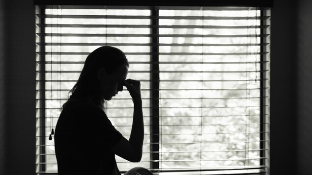 L'ombre d'une femme qui se tient la tête devant une fenêtre en noir et blanc.