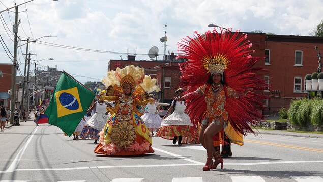 Deux femmes qui portent des costumes colorés dansent. L'une d'elles brandit un drapeau du Brésil.