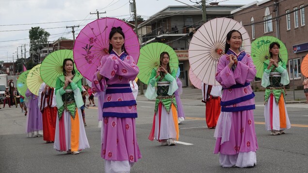 Des personnes en costumes traditionnels chinois marchent avec des ombrelles.