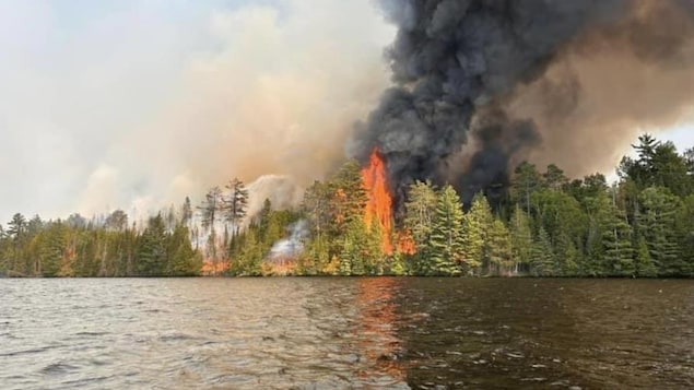 Une forêt en feu vue d'un cours d'eau.