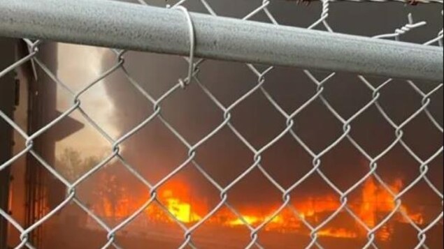 Une clôture de métal avec un incendie dernière qui boucane.  
