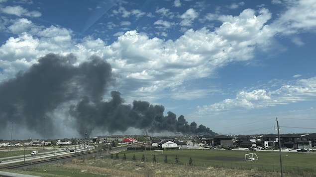 Des maisons résidentielles avec une énorme plume de fumée en arrière.