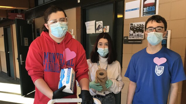 Trois jeunes élèves avec des masques et des produits de nettoyage.