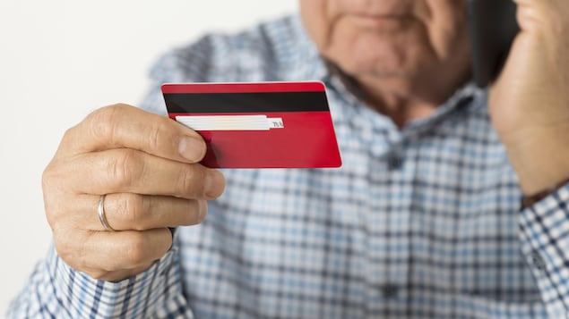 Un homme âgé parle au téléphone en tenant, dans son autre main, une carte de crédit.