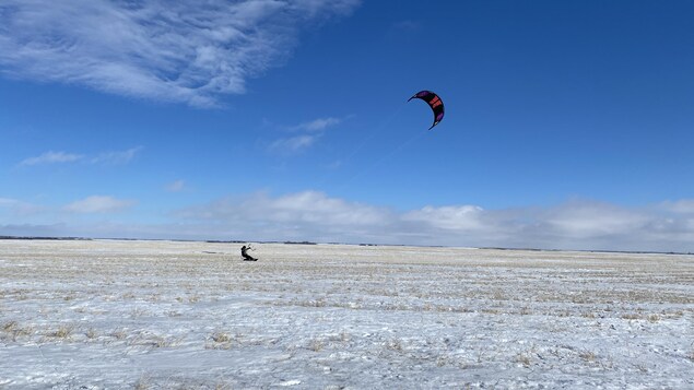 Un kitesurfer contre un ciel bleu. Il y a peu de neige dans le champ.
