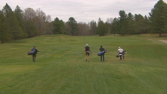 Quatre jeunes golfeurs marchent sur un terrain de golf. 